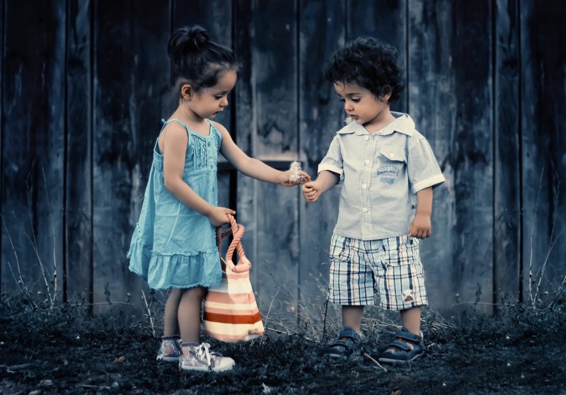 small girl and boy in front of blue fence