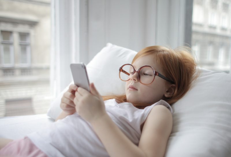 small girl with red hair and glasses looking at smartphone