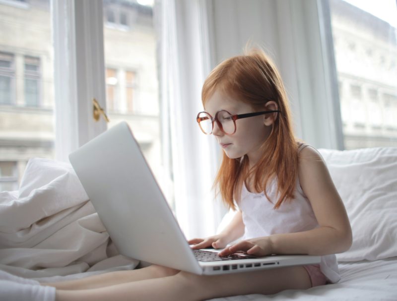 small girl with red hair and glasses looking at laptop